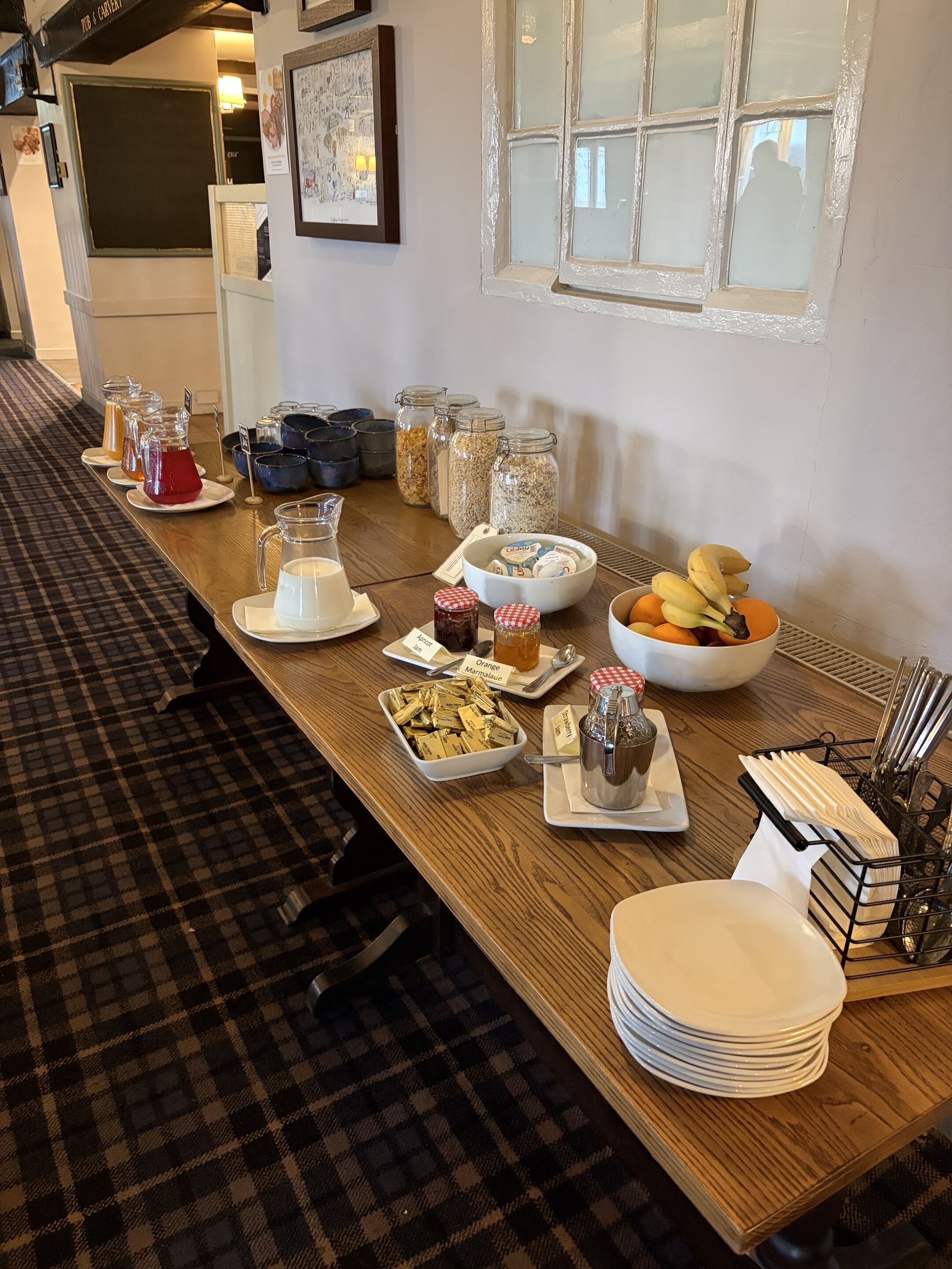 A buffet table with various food items and condiments, including jars of marmalade and a bowl of oranges.