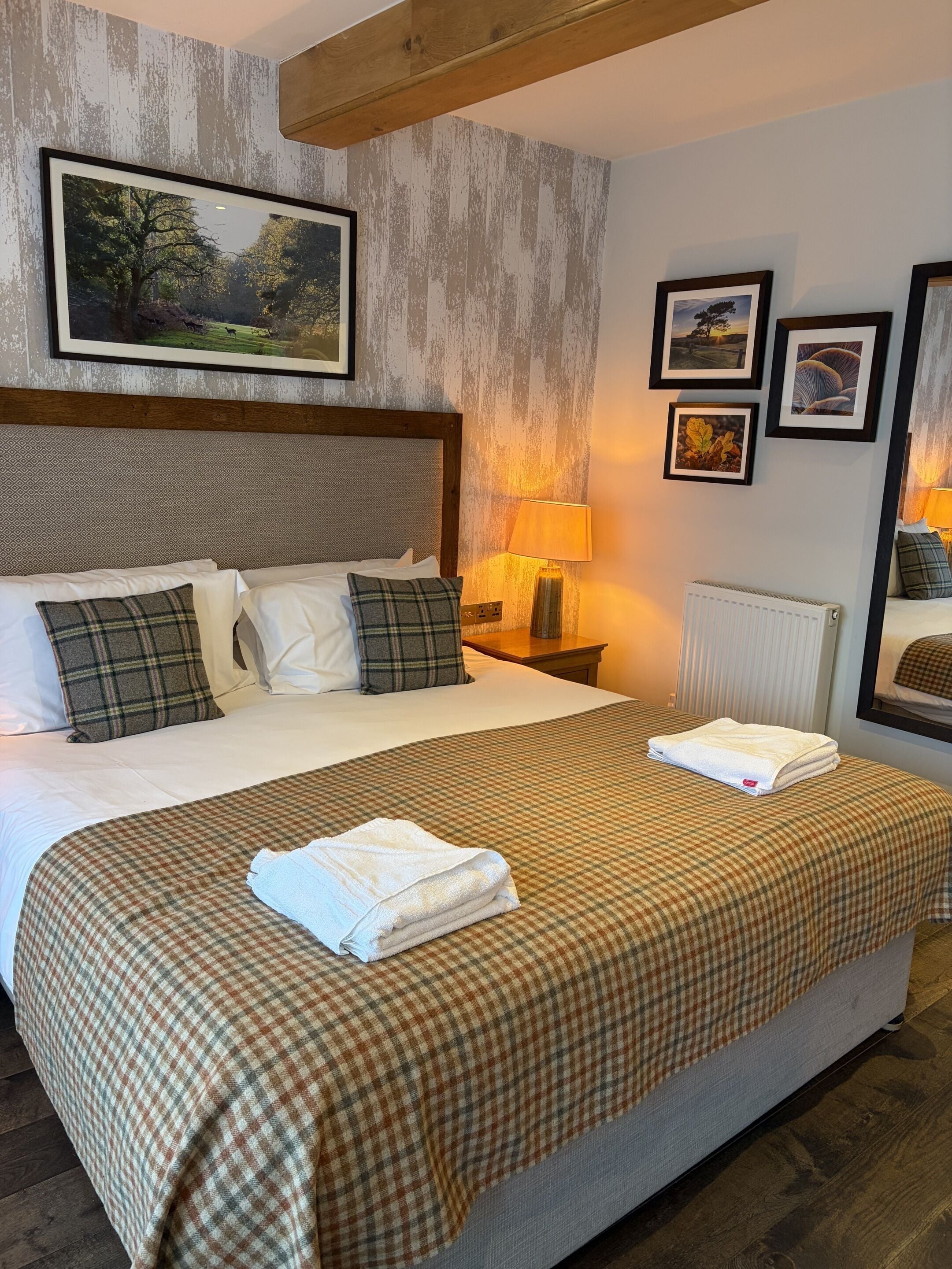 A neatly made bed with a plaid bedspread and two pillows, a bedside lamp, and framed pictures on the wall.
