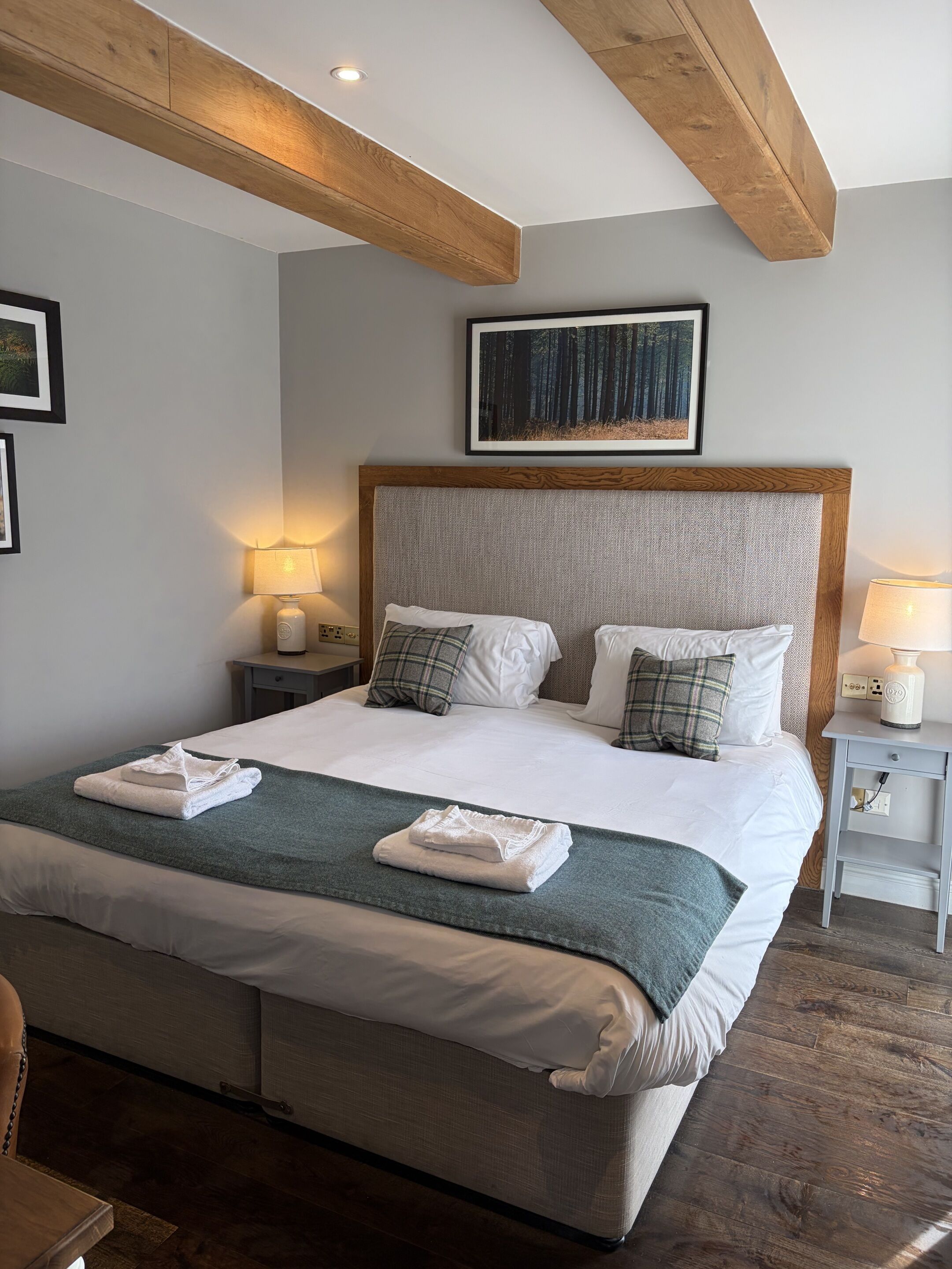 A neatly made bed with white linens and a green throw blanket, wooden headboard, and two bedside lamps.