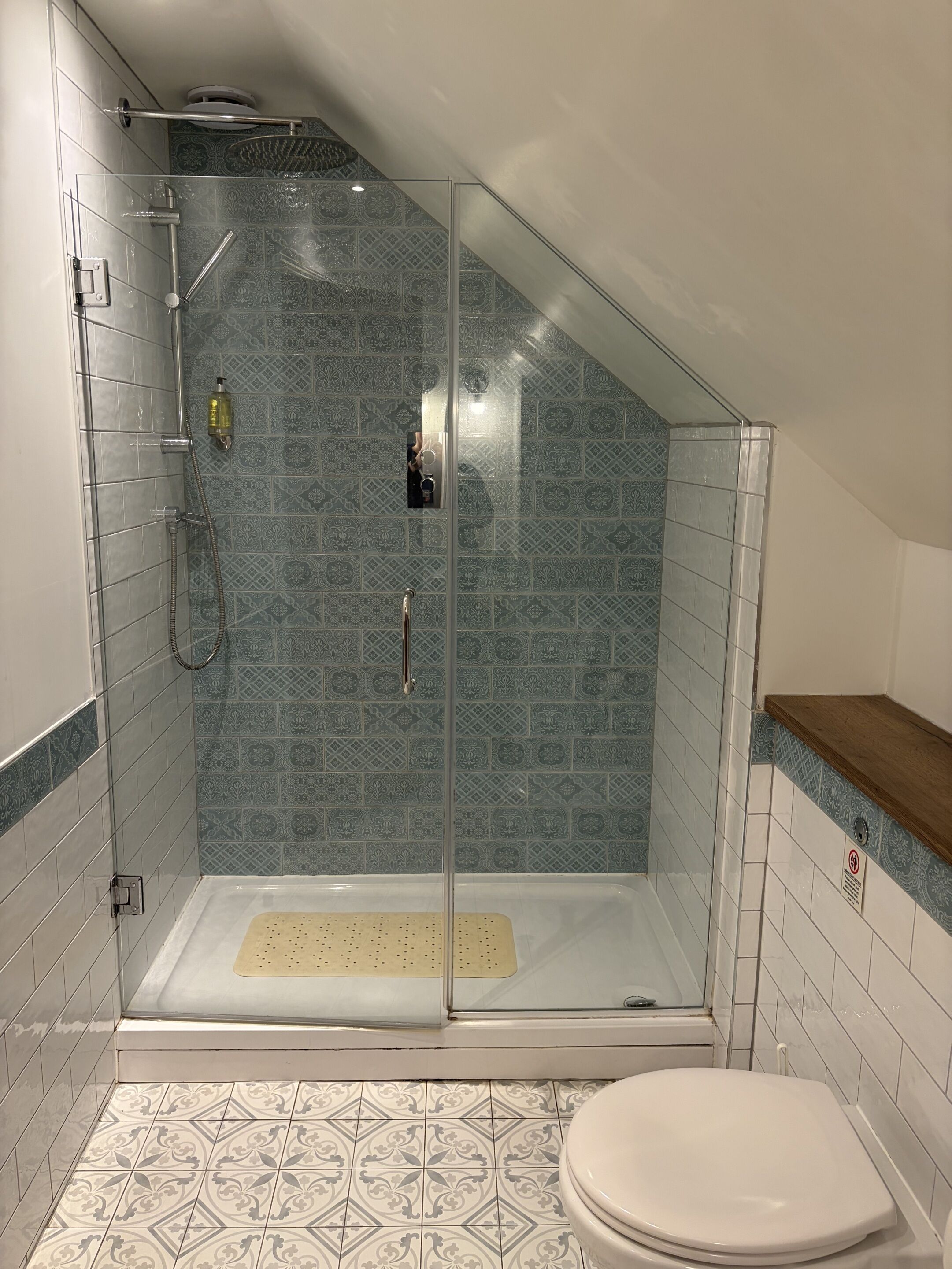 A shower with a glass door, a toilet, and patterned tiles.
