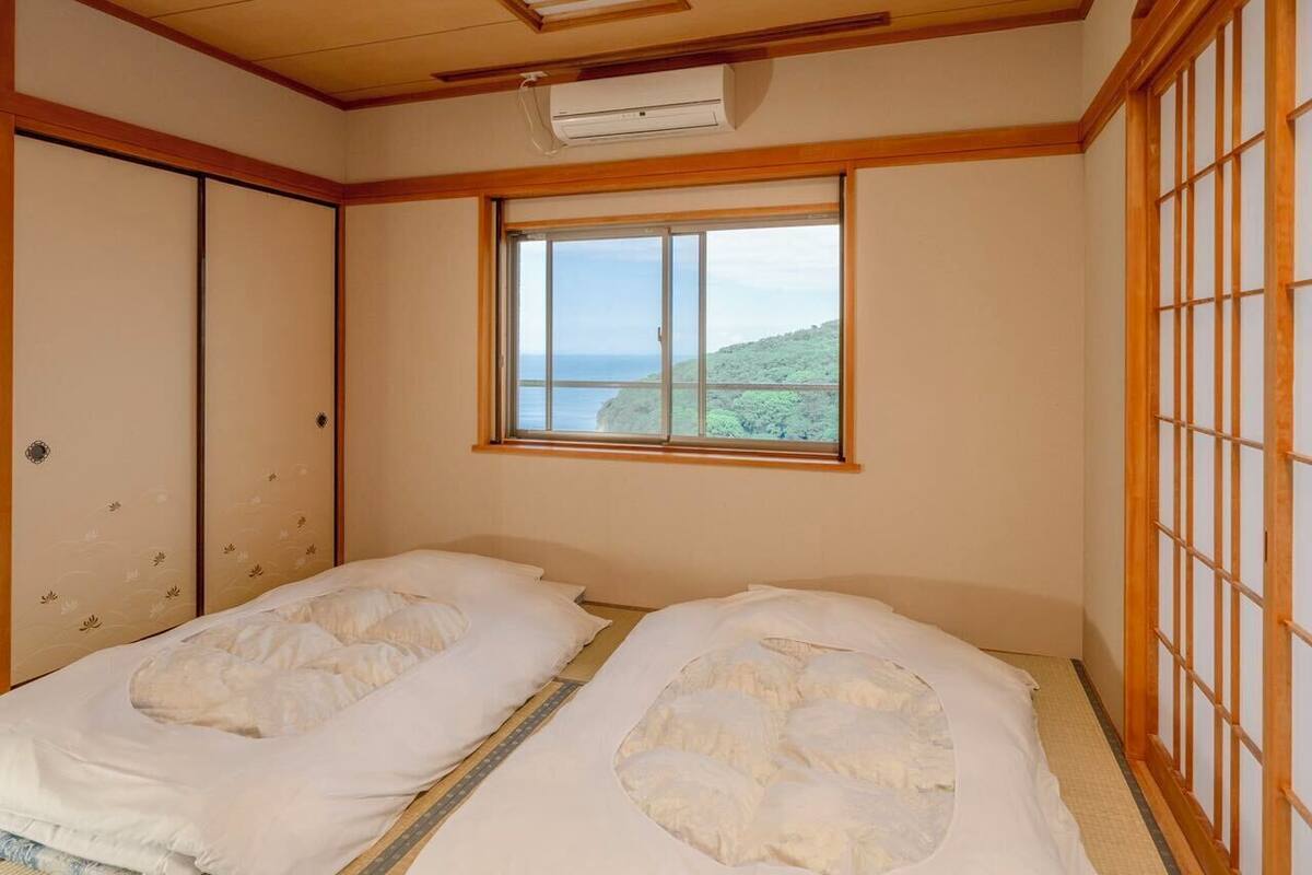 Um quarto japonês tradicional com tatames, dois tatames, uma janela com vista para o mar e um ventilador de teto.