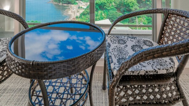 A balcony with wicker furniture, a glass table, and a view of a coastal landscape. - Manazuru Marin (Manazuru)