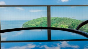 A clear view of a tropical island with lush greenery and a calm sea, viewed through a window with a metal railing. - Manazuru Marin (Manazuru)