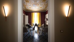 Habitación de hotel con zona de comedor que incluye una mesa, sillas, una araña y suelo estampado.