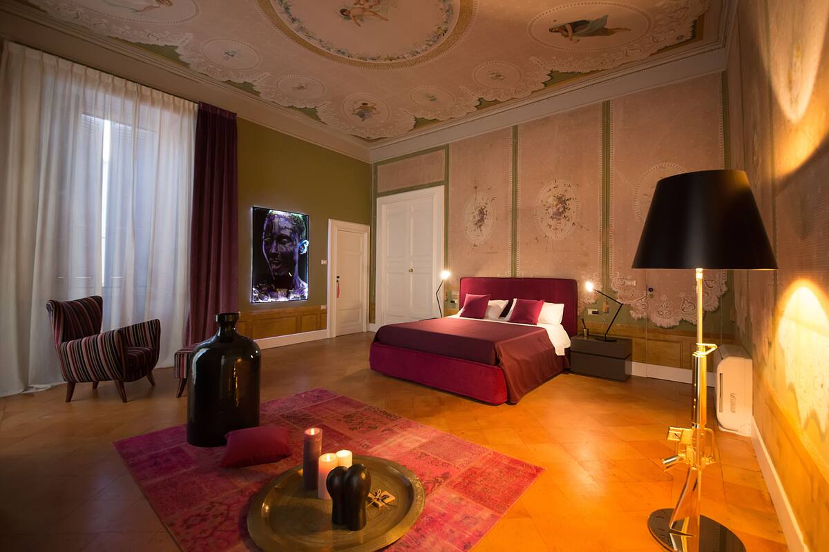 A bedroom with a large bed, a chair, a table with candles, and a lamp.