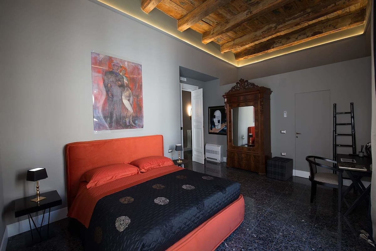 A bedroom with a large bed, a desk, a chair, a mirror, and a painting on the wall.