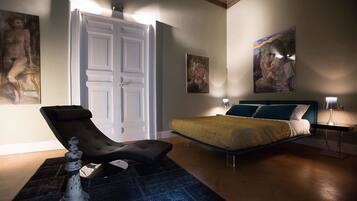 A bedroom with a bed, a reclining chair, a nightstand, and artwork on the walls.