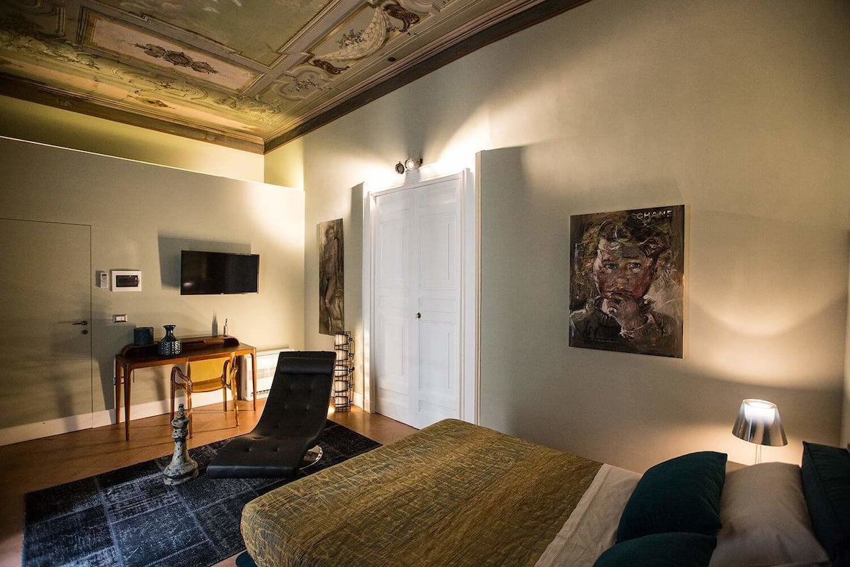 A hotel room with a bed, a desk, a chair, a TV, and artwork on the walls.