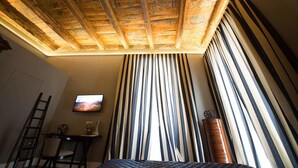 Una habitación con techo inclinado, una cama, un televisor, una silla, una mesa y cortinas a rayas.