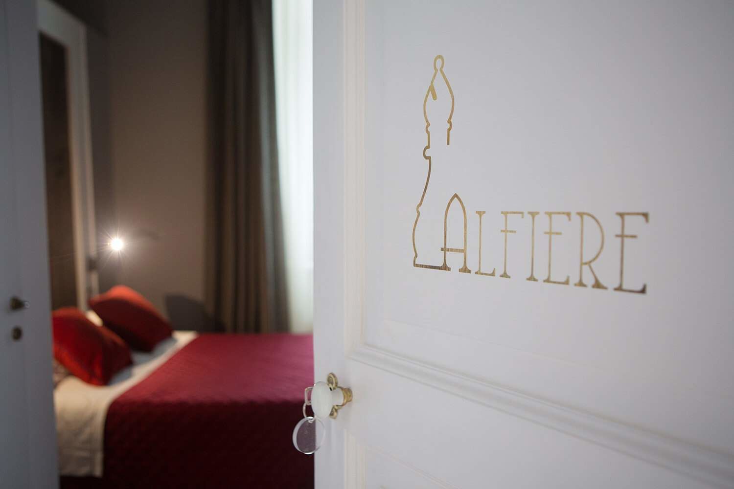 Ein Hotelzimmer mit einem Bett, roter Bettwäsche und einer Wand mit der Aufschrift 'ALFIERE' in goldener Schrift.