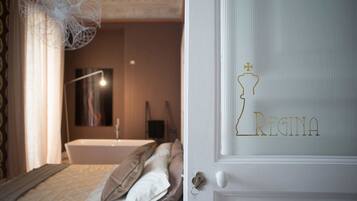 A bedroom with a bed, pillows, a bedside table, a mirror, and a wall-mounted light fixture.