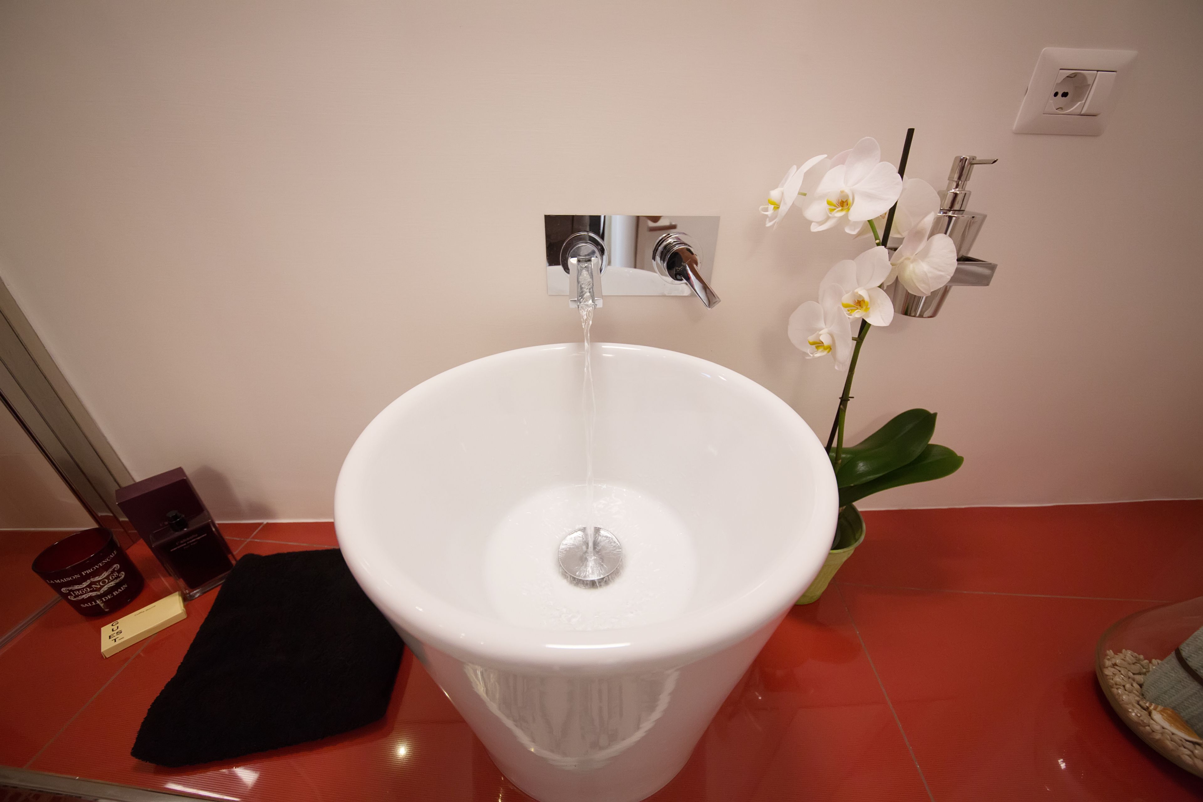 A white sink with a chrome faucet, a potted orchid, and a black towel on a red tiled floor.