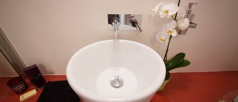 A white sink with a chrome faucet, a potted orchid, and a black towel on a red tiled floor.