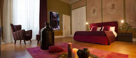 Un dormitorio con una cama grande, una silla, una mesa con velas y un cuadro en la pared.