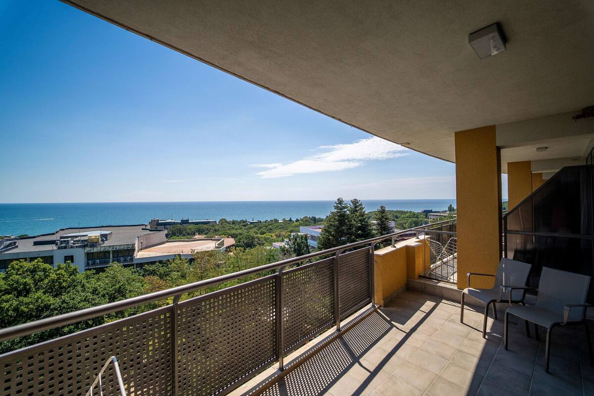 A balcony with a view of the sea, a railing, and two chairs.