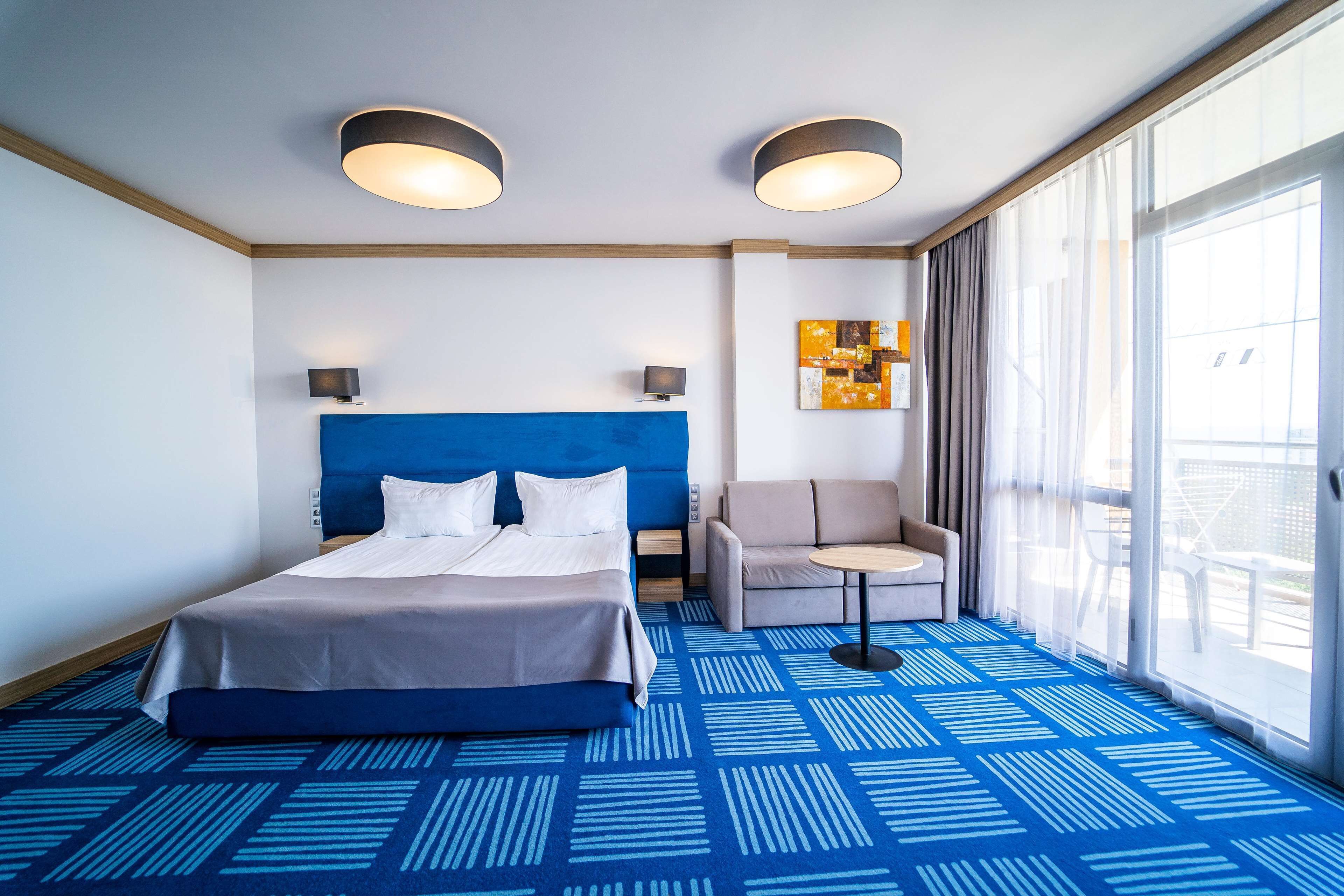 Een hotelkamer met een groot bed, een slaapbank, een tafeltje en een groot raam met gordijnen.