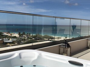 A balcony with a glass railing overlooking a beach and ocean.