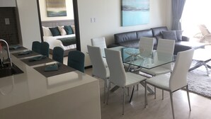 Una sala de estar moderna con una mesa de comedor de vidrio, sillas blancas, un sofá y un cuadro grande en la pared.