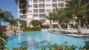 Un hotel con piscina rodeada de palmeras y sillas de descanso.