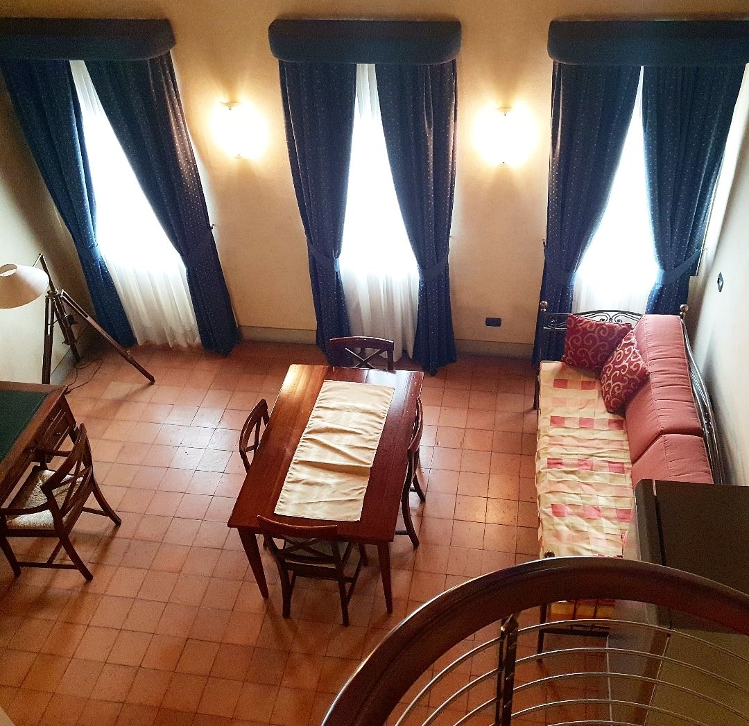 Un coin repas avec une table et des chaises en bois, un canapé et un lit. Il y a des rideaux aux fenêtres et une lampe sur le côté gauche.