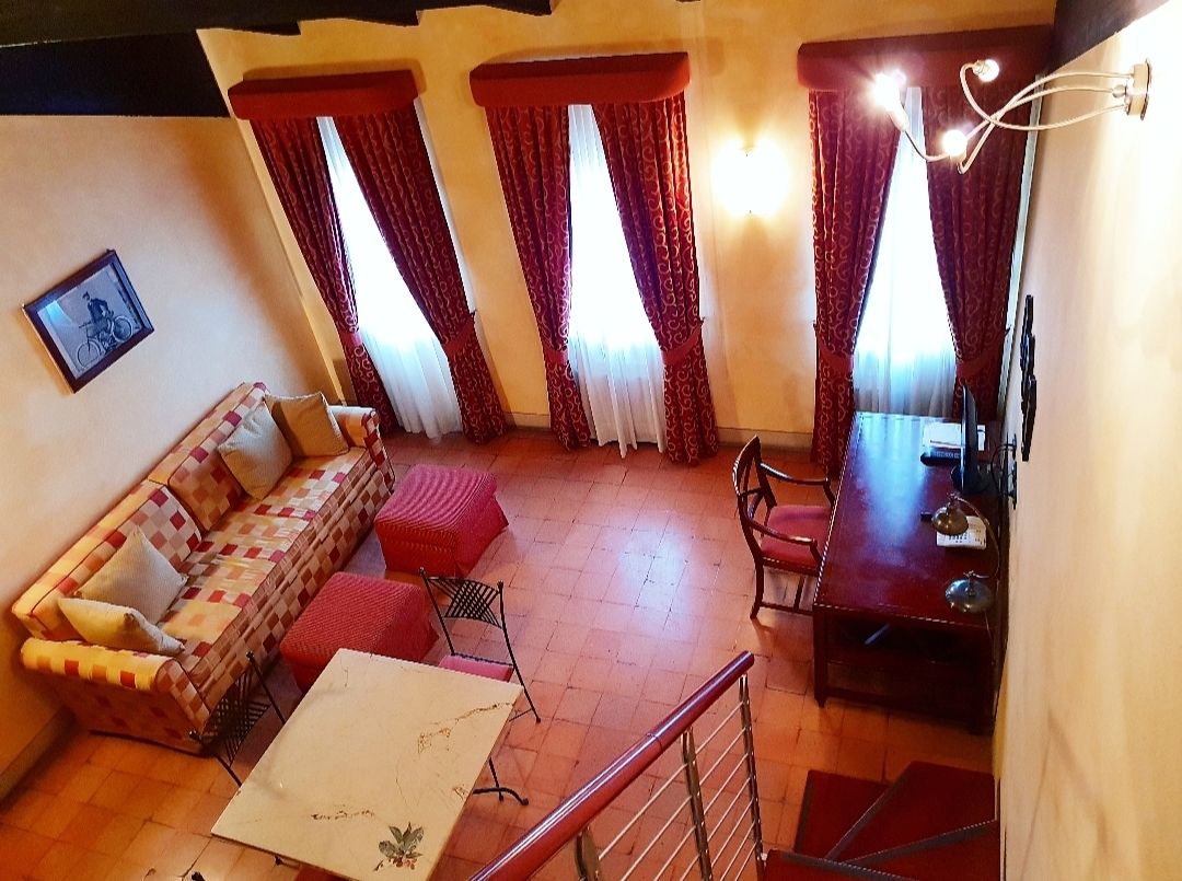 A cozy living area with a sofa, a dining table, and chairs. There are curtains on the windows, and a picture frame is visible on the wall.
