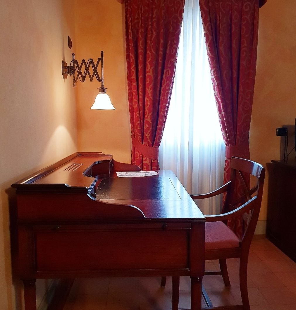 A dining area with a wooden table and chairs, a wall-mounted light fixture, and red patterned curtains.