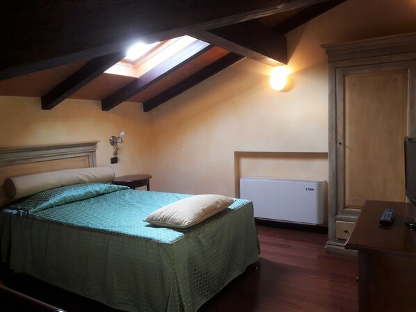A bedroom with a bed, a nightstand, a lamp, a radiator, and a wardrobe.