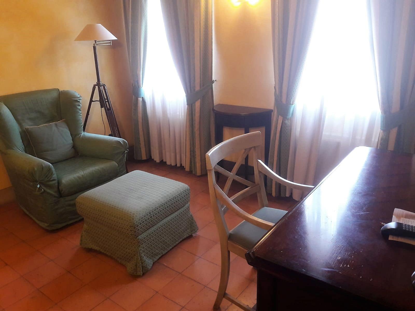Una stanza con una poltrona verde, un poggiapiedi, un tavolo da pranzo in legno e una lampada da terra.