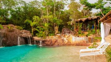 A pool area with a waterfall, lounge chairs, and a thatched-roof structure.