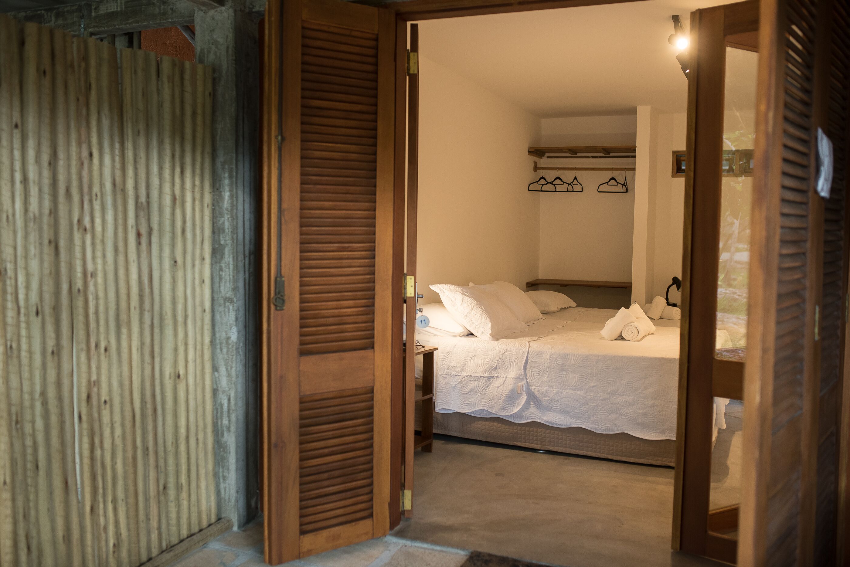 A bedroom with a bed, a wooden door, and a white wall with a coat rack.