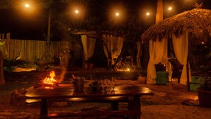 An outdoor dining area with a fire, wooden furniture, and string lights. - Pousada Caminho das Cachoeiras (Alto Paraíso de Goiás)