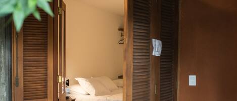 A room with a bed, a table, and a chair. There is a door leading to another room.