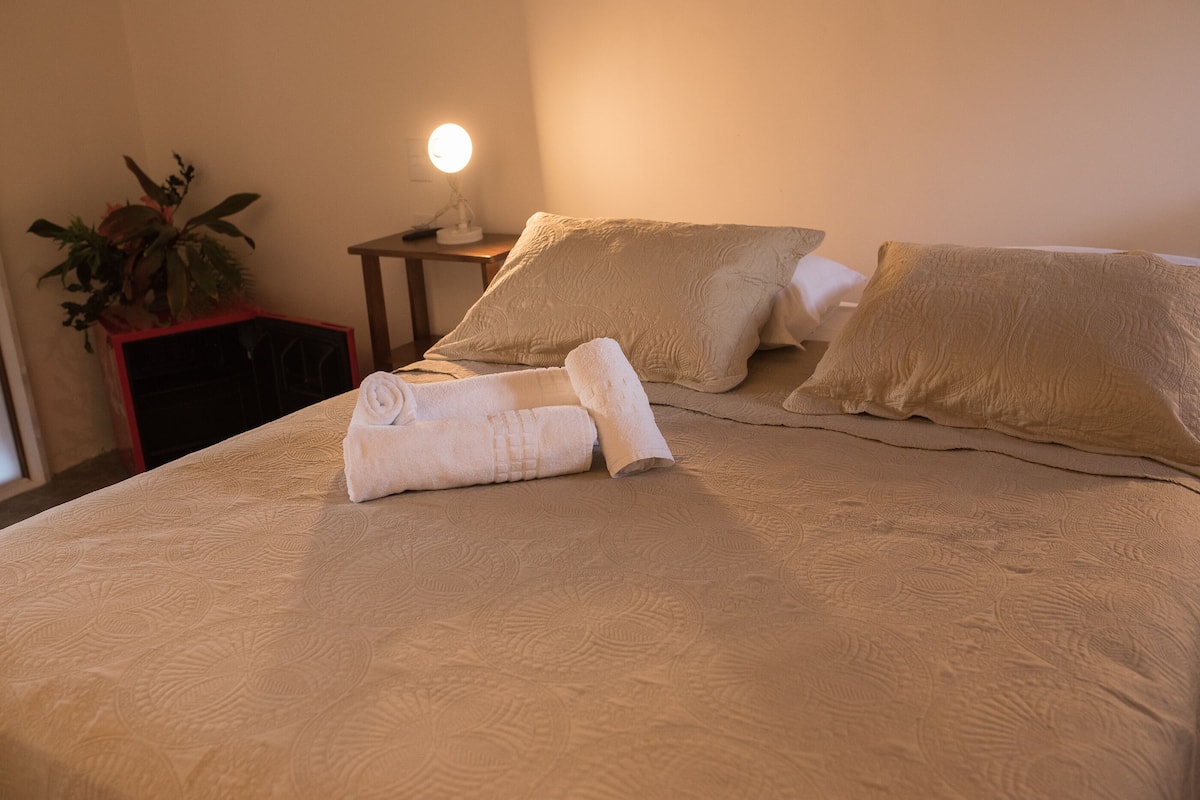 A neatly made bed with a beige bedspread, two pillows, and a rolled towel.