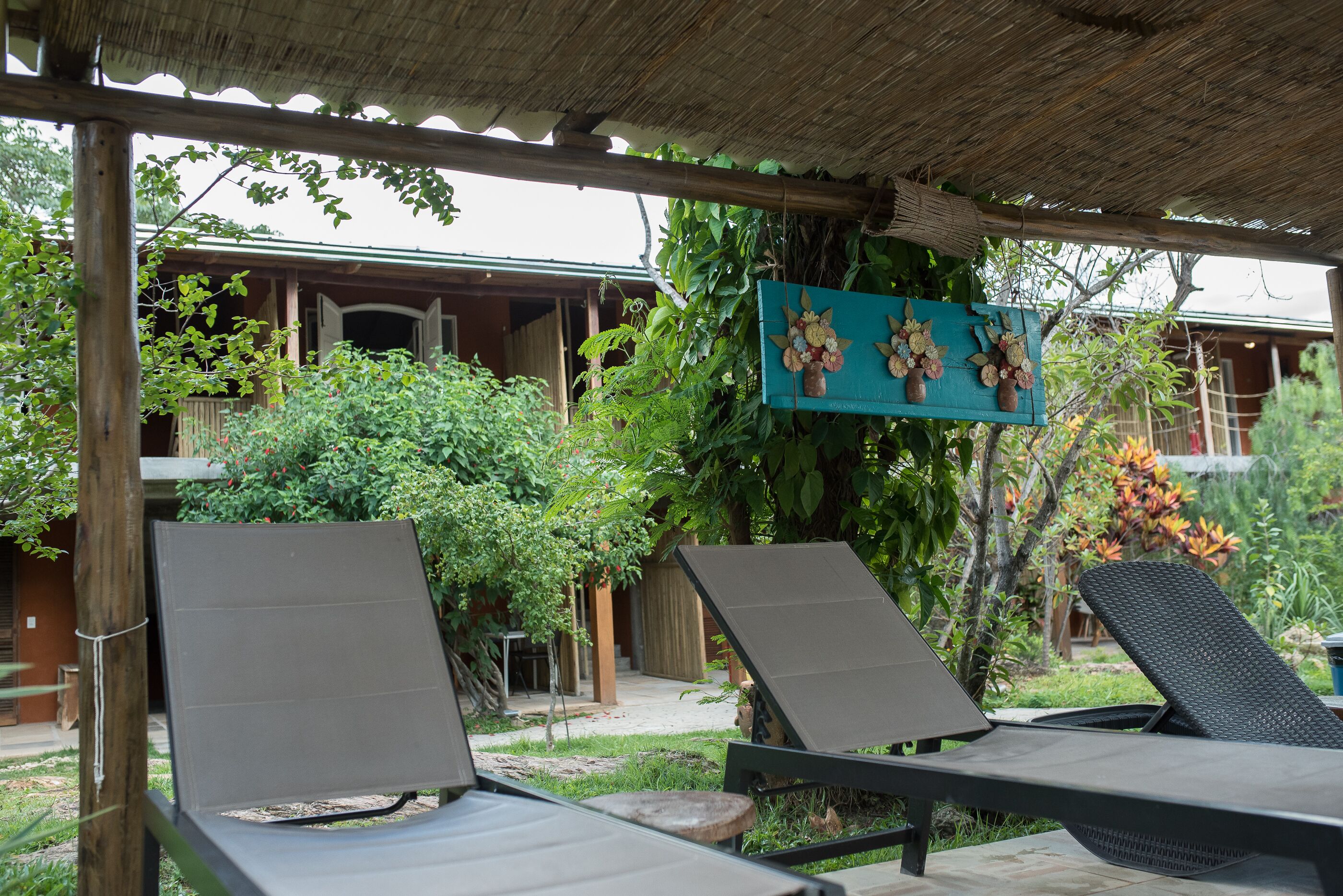 A covered outdoor seating area with two lounge chairs and a hanging flower arrangement.