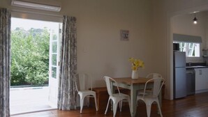 Ein Zimmer mit Esstisch, Stühlen, einer kleinen Küchenzeile und Blick ins Grüne.