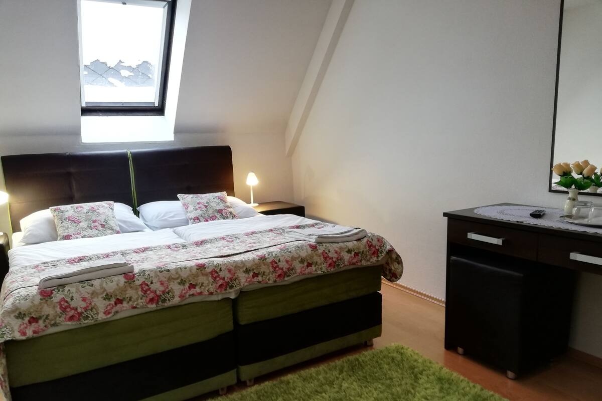 Ett sovrum med en säng, sängbord, ett skrivbord, en spegel och ett fönster.
