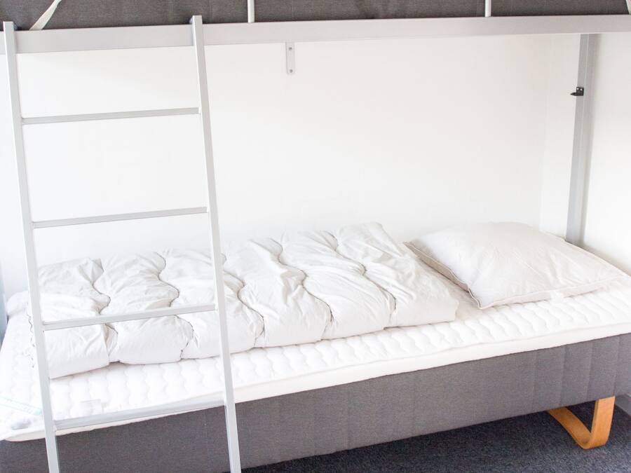 Una cama individual superpuesta con escalera, un colchón gris y una almohada blanca.