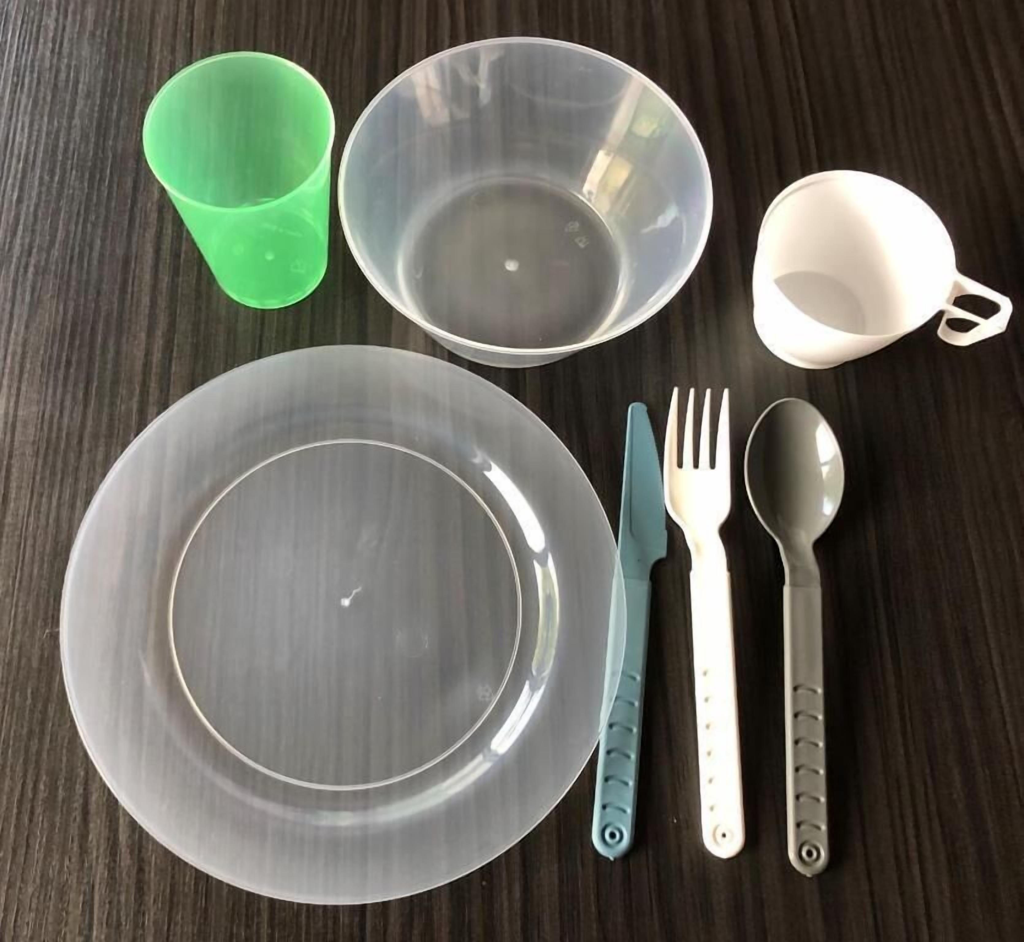 Una mesa con un plato, una taza verde, una taza blanca, un cuchillo, un tenedor y una cuchara.