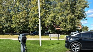 Un estacionamiento con estación de carga para vehículos eléctricos, zona verde y sendero pavimentado.