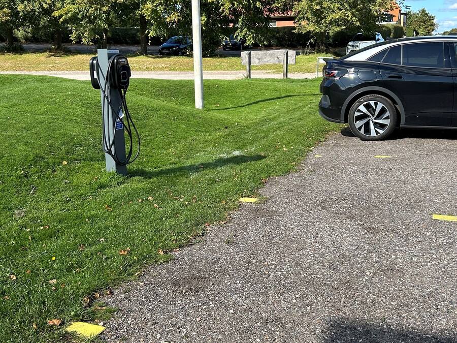 En parkeringsplats med en laddstation för elfordon, en gräsyta och en asfalterad gångväg.