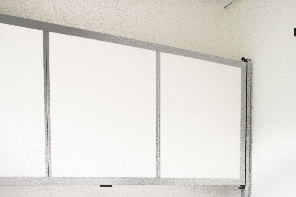 A single bed with a grey upholstered headboard, a white mattress, and a grey carpeted floor.