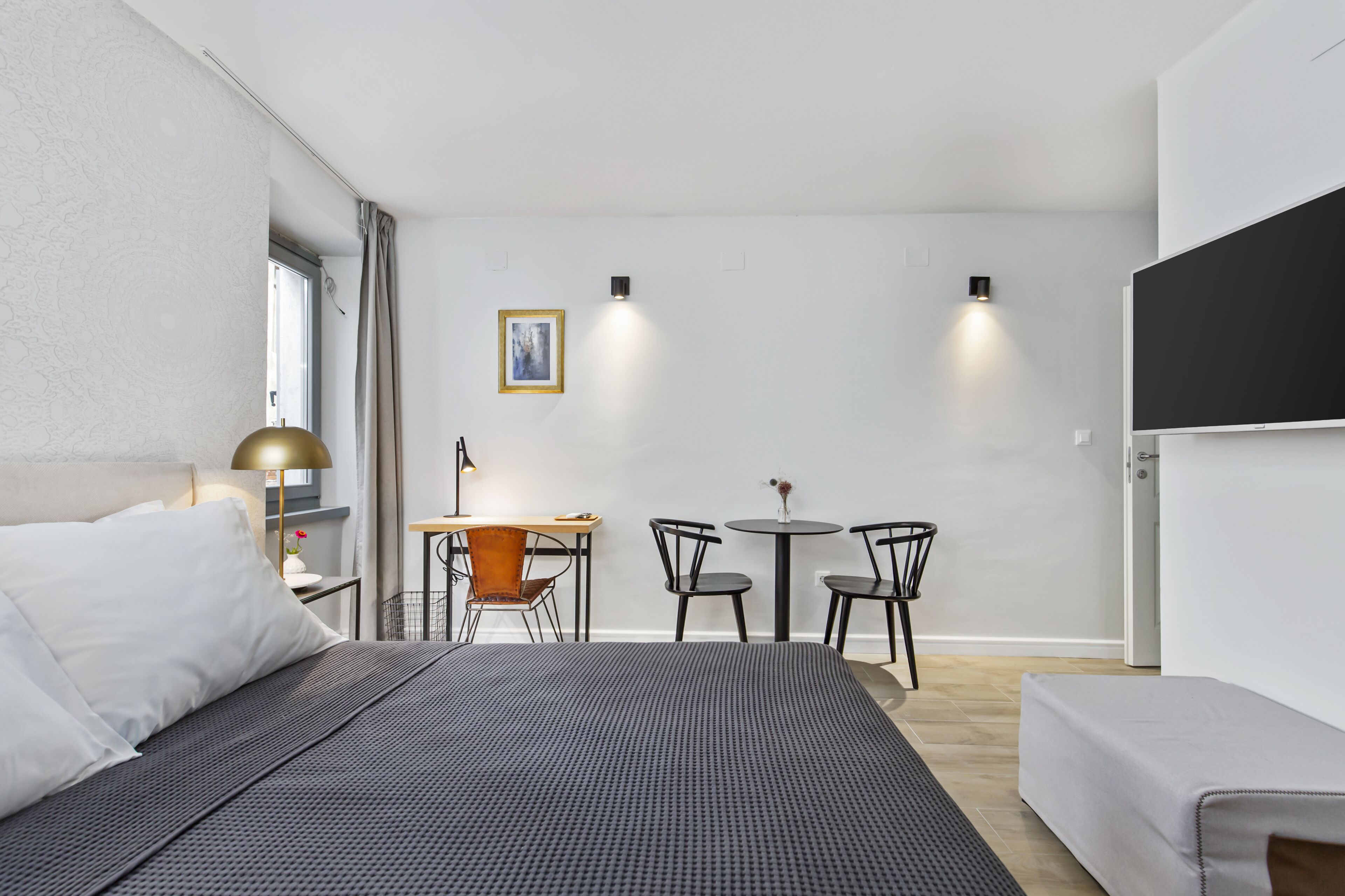 Une chambre d’hôtel moderne avec un grand lit, un bureau avec deux chaises, une petite table et un tableau au mur.
