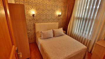 A bedroom with a bed, two wall-mounted lights, a door, and a window with curtains.