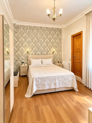 A bedroom with a large bed, two bedside tables, a wooden door, and a patterned wallpaper. - Mimoza Butik Otel Buyukada (Adalar)