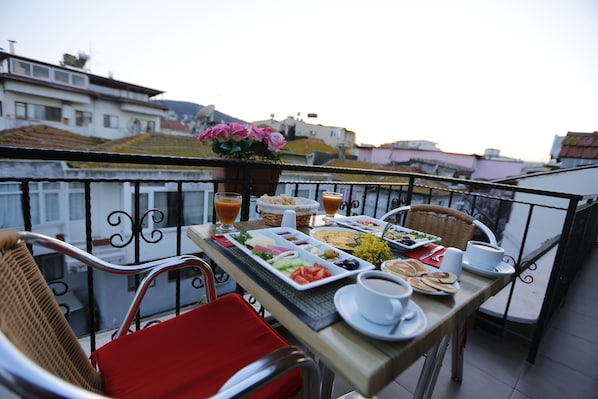 A balcony with a table set for breakfast, including plates of food, cups, and a potted plant.