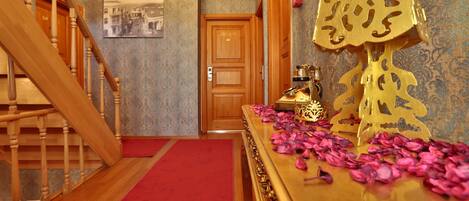 A hallway with a wooden staircase, a red carpet, a gold decorative piece, and a door with a vintage photograph on the wall.