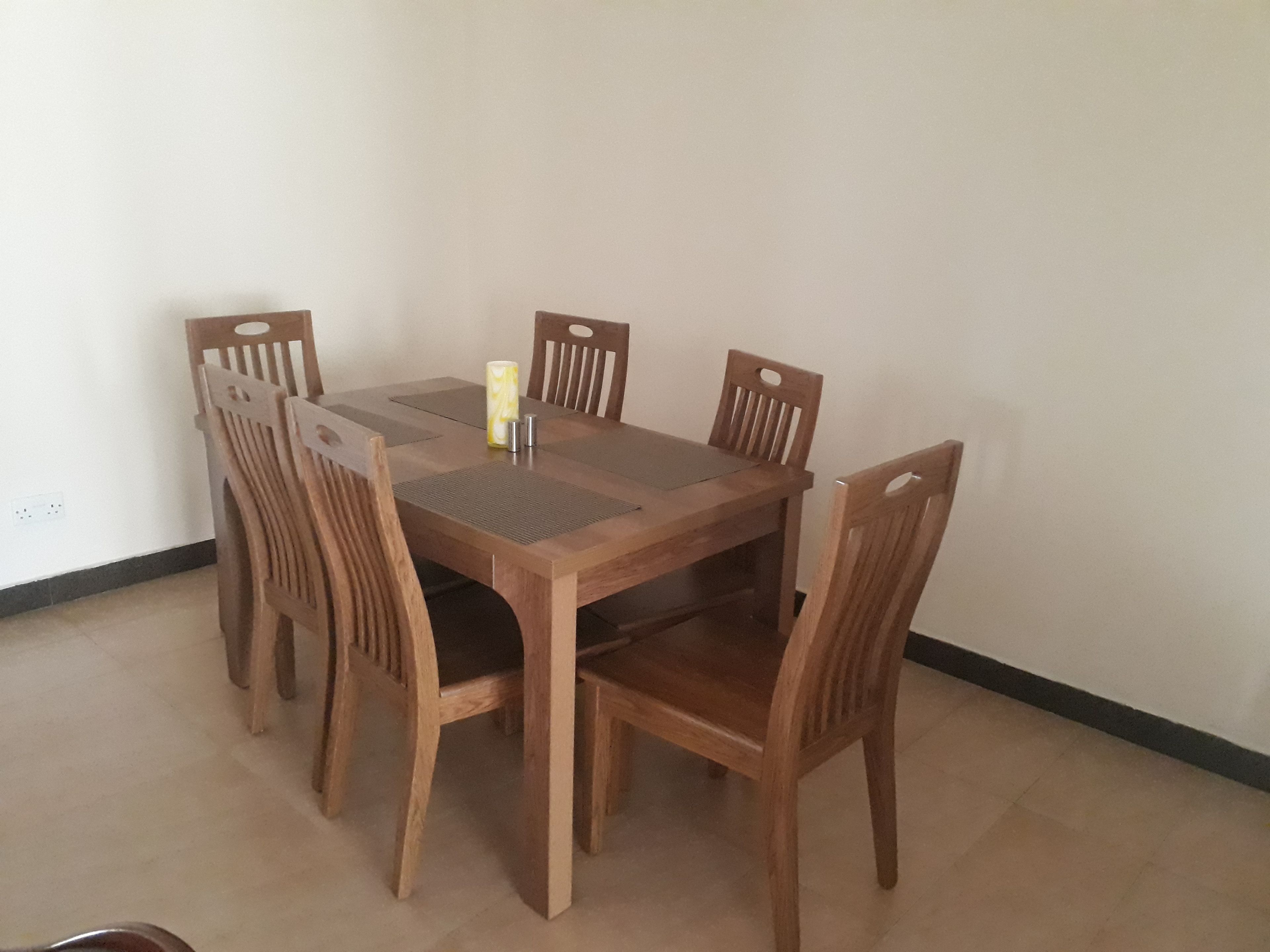 A rectangular wooden dining table with six chairs, a small table runner, and a candle holder.