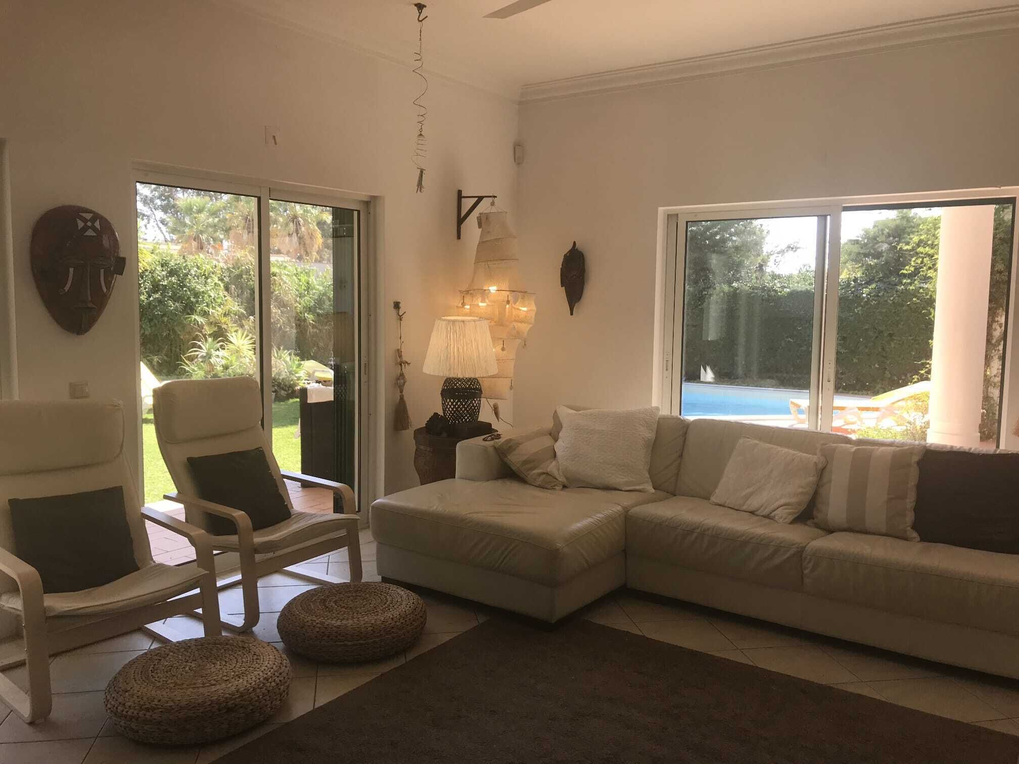 Ein Wohnzimmer mit einer Couch, Sesseln, einer Lampe und Blick auf einen Swimmingpool.
