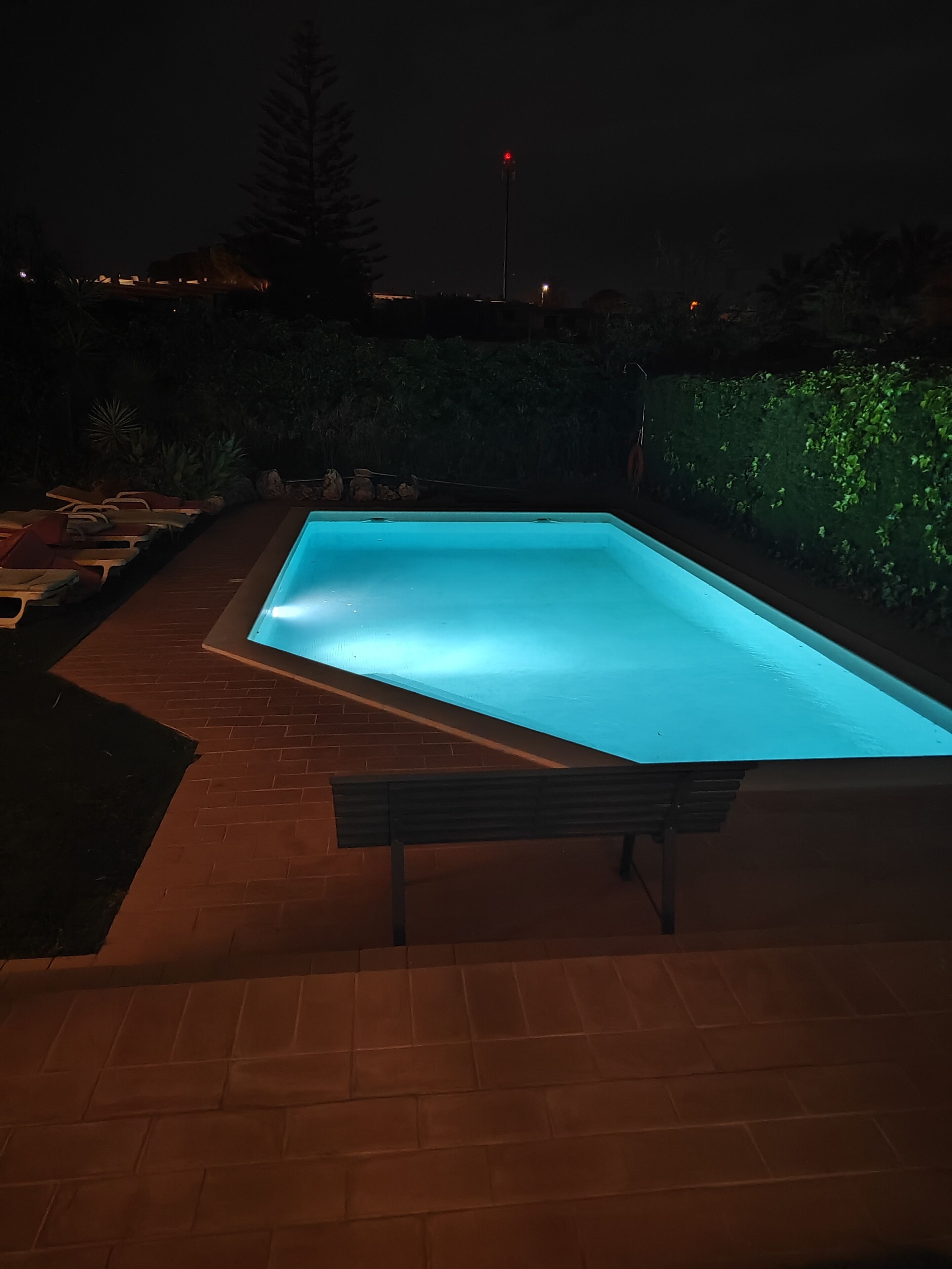 A rectangular swimming pool with a wooden deck and a bench.