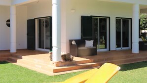 A covered outdoor seating area with a sofa and a yellow lounge chair, a stone planter, and a tiled patio. - Luxury Villa With Private Pool (Albufeira)